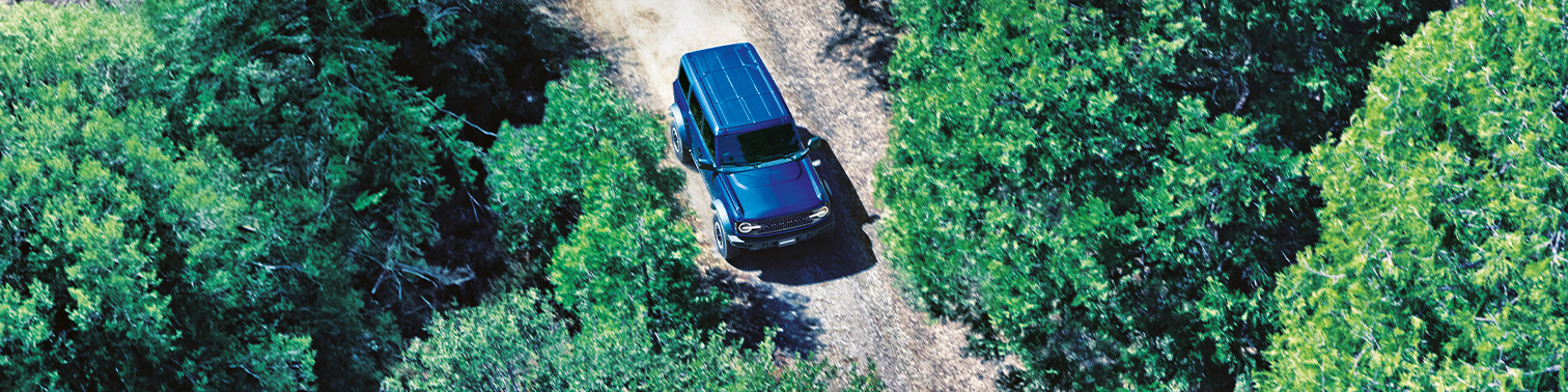 picture from above is showing a blue Bronco driving through the forest